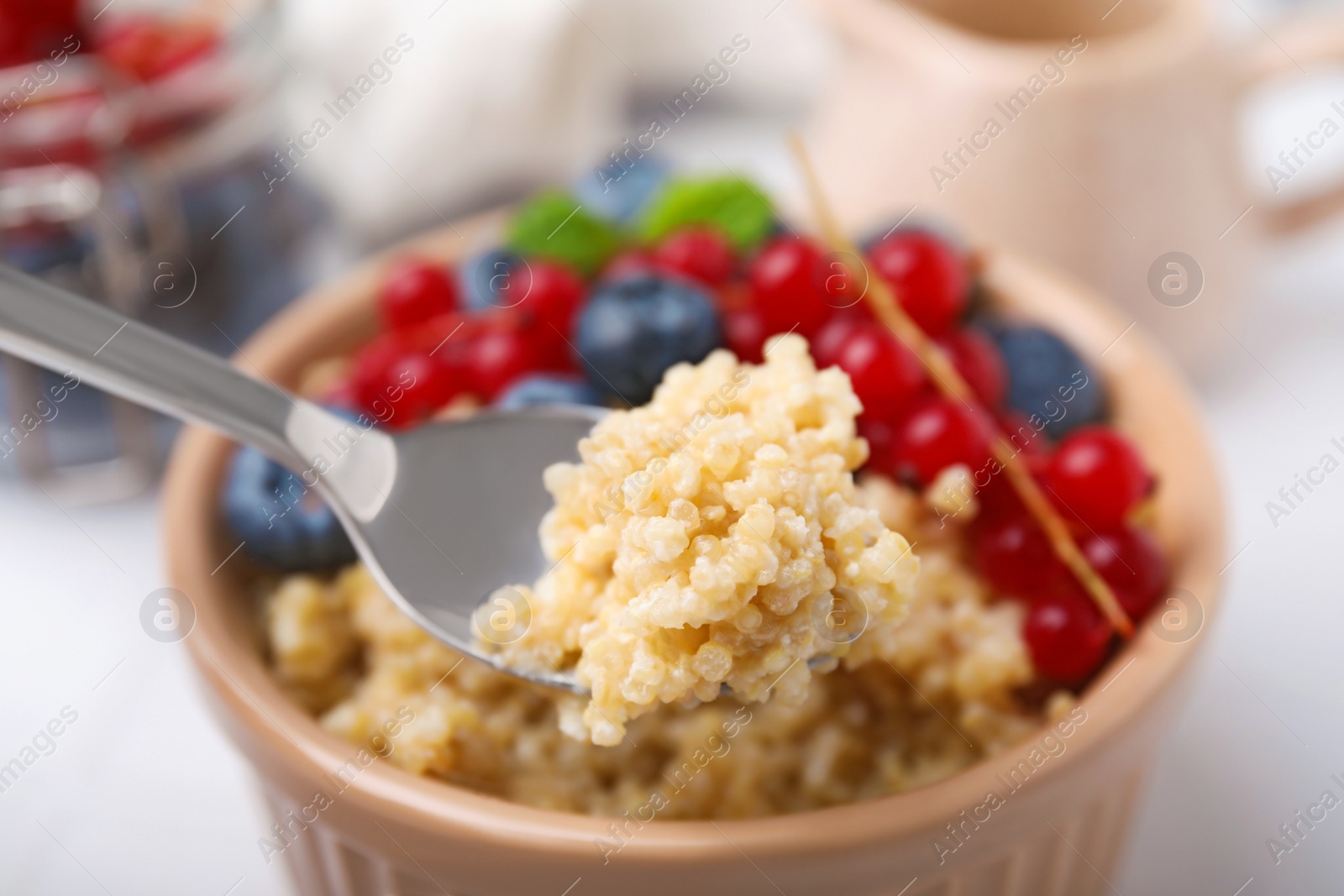 Photo of Spoon of delicious cooked quinoa above bowl, closeup