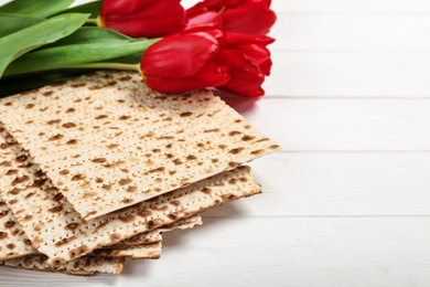 Photo of Traditional Pesach (Passover Seder) matzo and tulips on white wooden table. Space for text