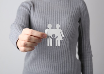 Photo of Woman holding paper silhouette of family on grey background, closeup. Life insurance concept