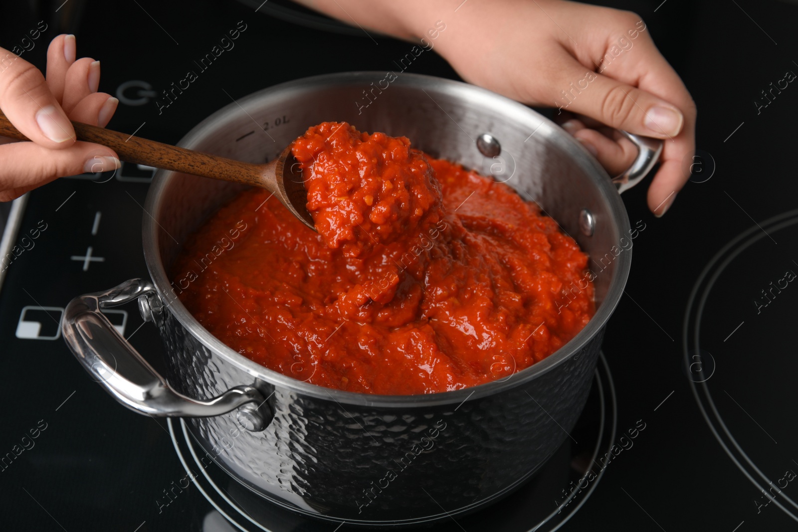 Photo of Woman cooking delicious tomato sauce in pan on stove, closeup