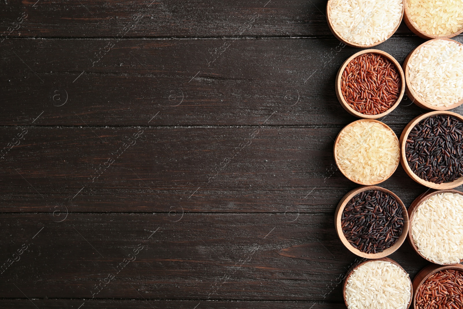 Photo of Flat lay composition with brown and other types of rice in bowls on wooden background. Space for text