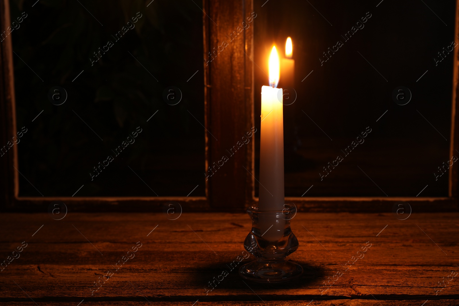 Photo of Burning candle on wooden table near window at night