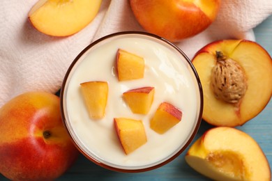 Photo of Tasty peach yogurt with pieces of fruit in glass on light blue wooden table, flat lay