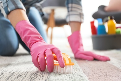 Photo of Woman cleaning carpet with brush in living room, closeup