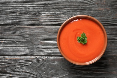 Photo of Bowl with fresh homemade tomato soup and space for text on wooden background, top view