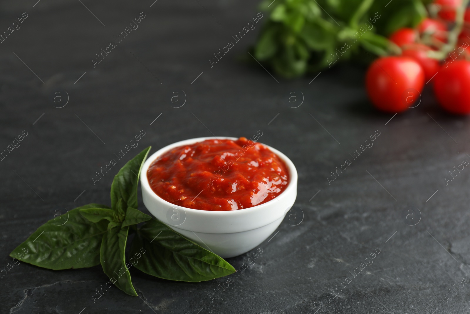 Photo of Delicious adjika sauce in bowl with basil on black table