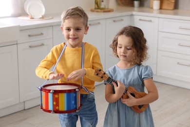 Little children playing toy musical instruments in kitchen