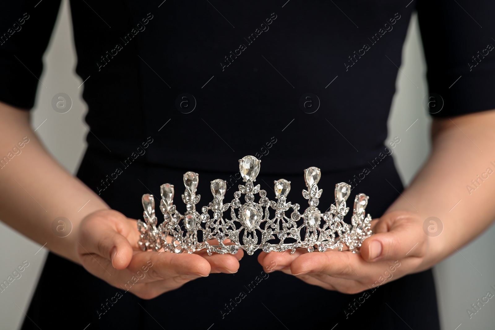 Photo of Woman holding luxurious tiara on grey background, closeup view