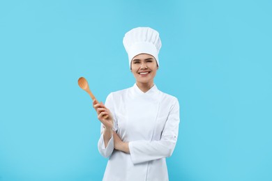 Photo of Happy chef with wooden spoon on light blue background