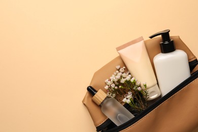 Preparation for spa. Compact toiletry bag with different cosmetic products and flowers on beige background, top view. Space for text