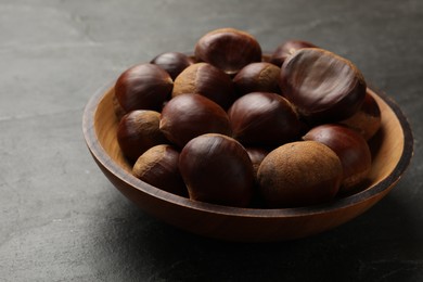 Photo of Roasted edible sweet chestnuts in bowl on grey table, closeup