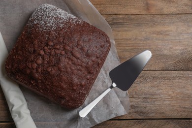 Photo of Homemade chocolate sponge cake and spatula on wooden table, flat lay. Space for text
