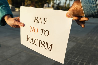 Photo of Woman and African American man holding sign with phrase Say No To Racism outdoors, closeup