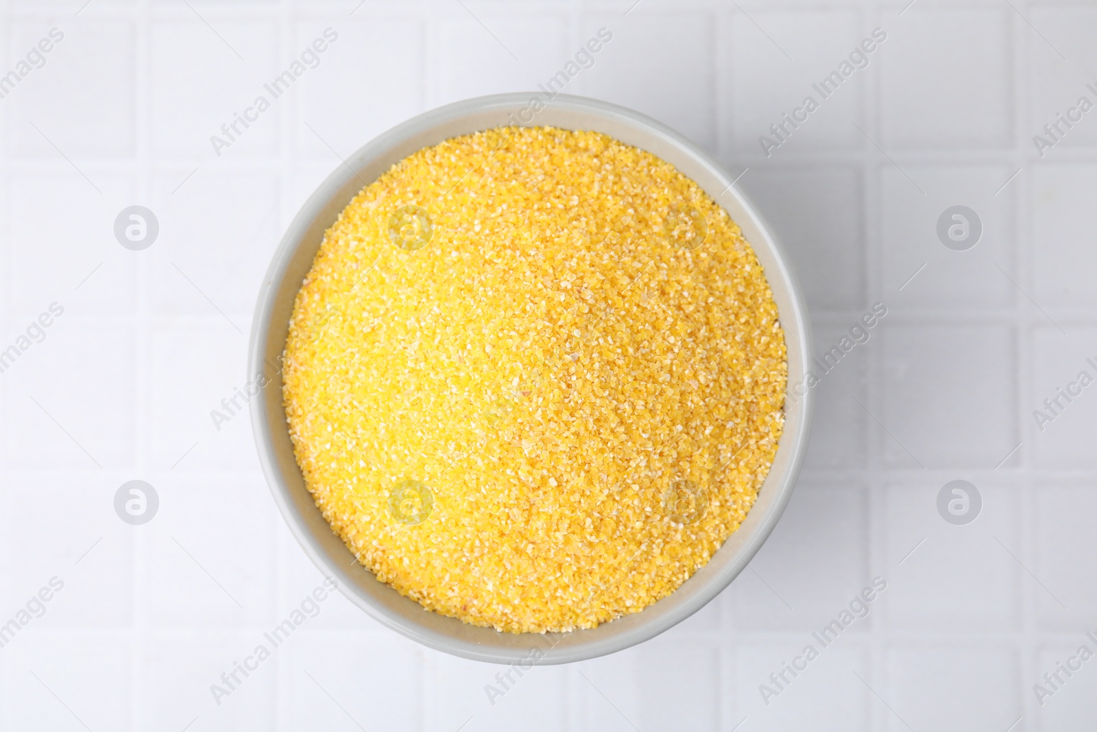 Photo of Raw cornmeal in bowl on white tiled table, top view