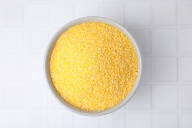 Raw cornmeal in bowl on white tiled table, top view