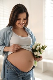 Photo of Young pregnant woman with flowers at home