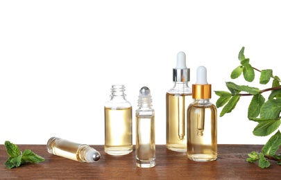 Bottles of mint essential oil on wooden table against white background. Space for text