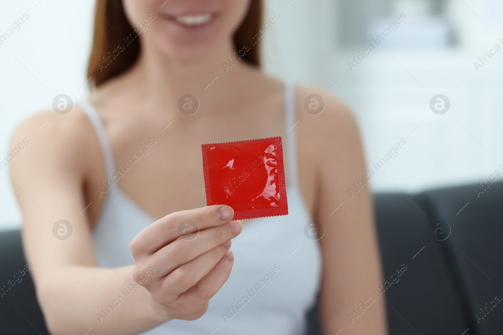 Photo of Woman holding condom indoors, closeup. Safe sex