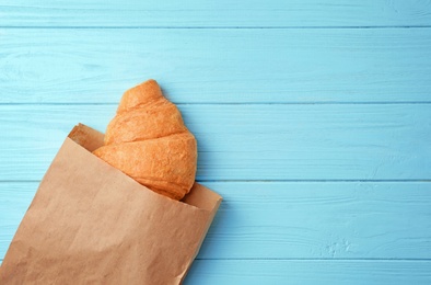 Photo of Tasty croissant in paper bag on wooden background, top view