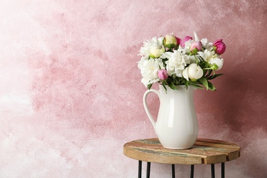 Vase with bouquet of beautiful flowers on table against color background