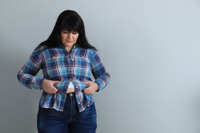 Overweight woman in tight shirt on light grey background. Space for text