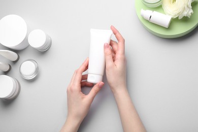 Woman holding tube of cream on light background, top view