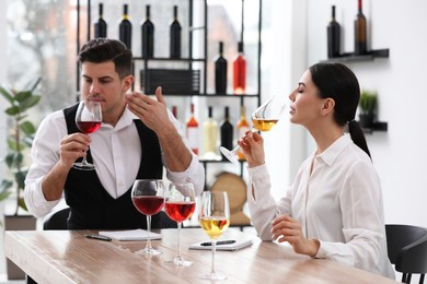 Photo of Sommeliers tasting different sorts of wine at table indoors