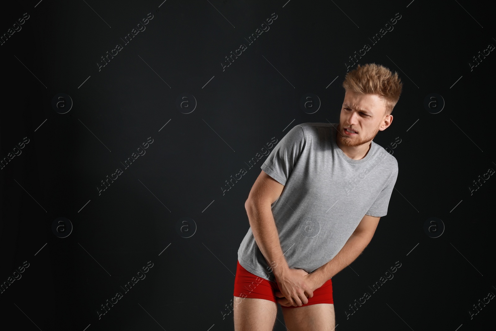 Photo of Young man suffering from pain on black background, space for text. Urology problems