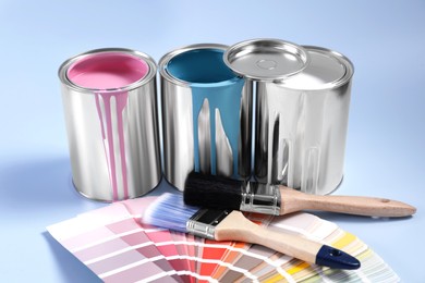 Photo of Cans of paints, palette and brushes on light blue background