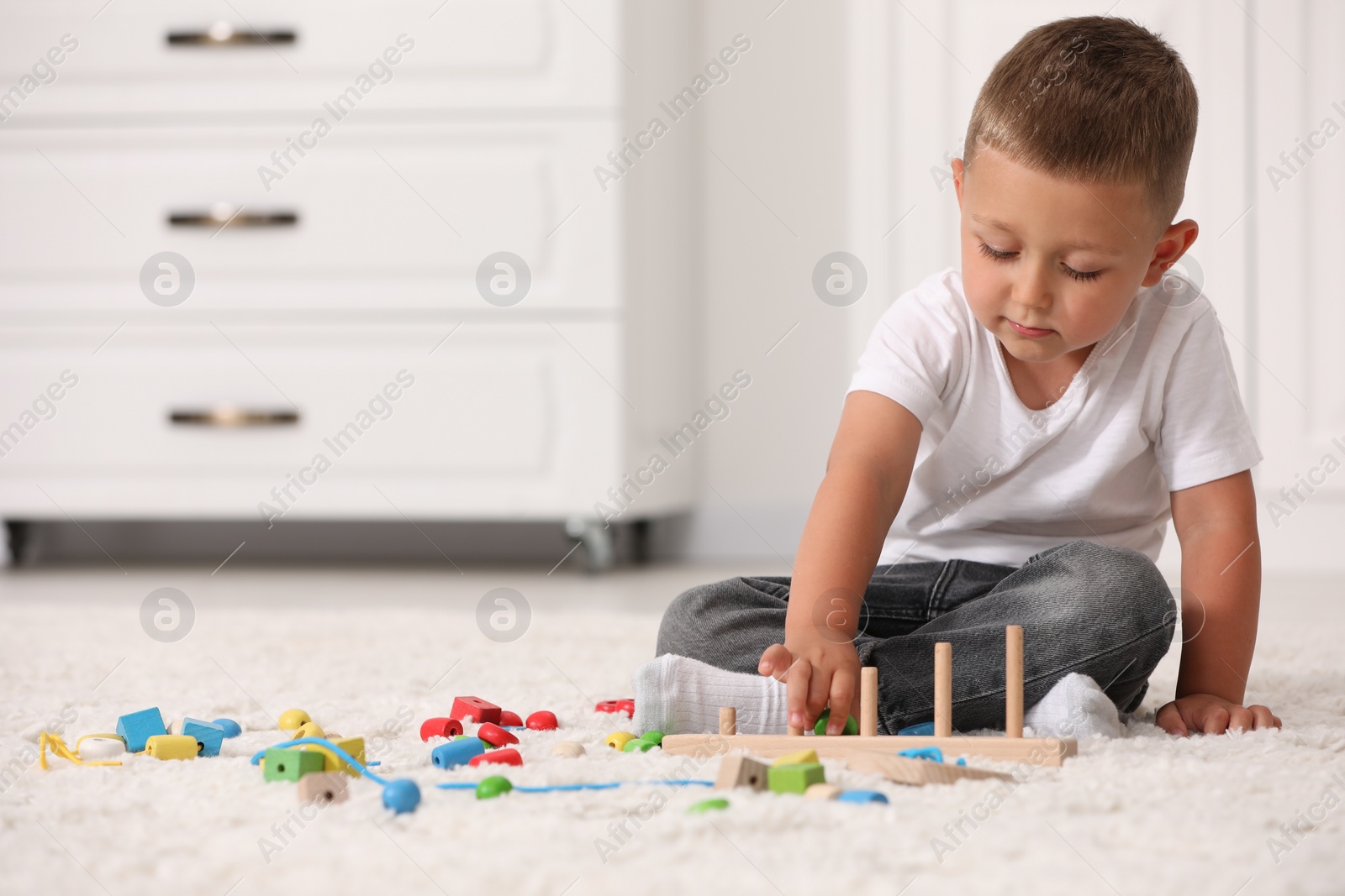 Photo of Motor skills development. Little boy playing with stacking and counting game on floor indoors