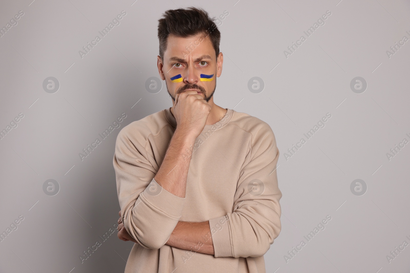 Photo of Angry man with drawings of Ukrainian flag on face against light grey background