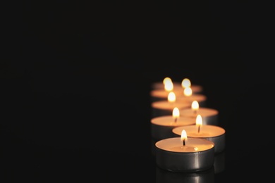Photo of Many burning candles on black table in darkness. Space for text