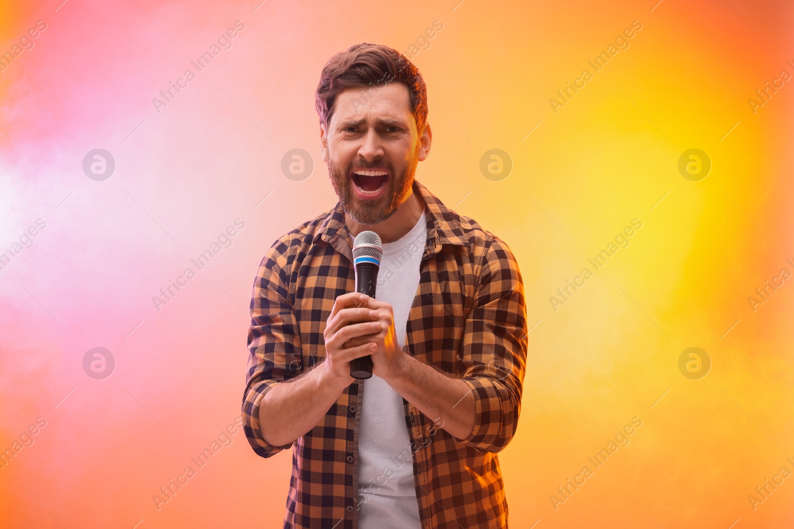 Photo of Handsome man with microphone singing in color lights