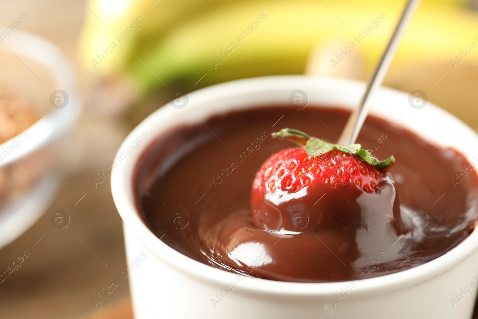 Photo of Dipping strawberry into fondue pot with chocolate, closeup