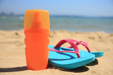 Photo of Sunscreen and flip flops on sandy beach. Sun protection care