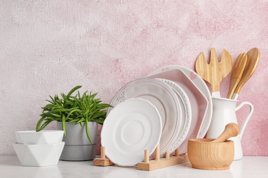 Green plant and different kitchenware on table near color wall. Modern interior design