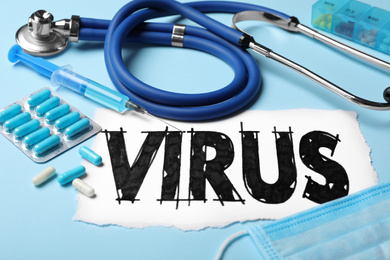 Photo of Word VIRUS, stethoscope and medicines on light blue background, closeup
