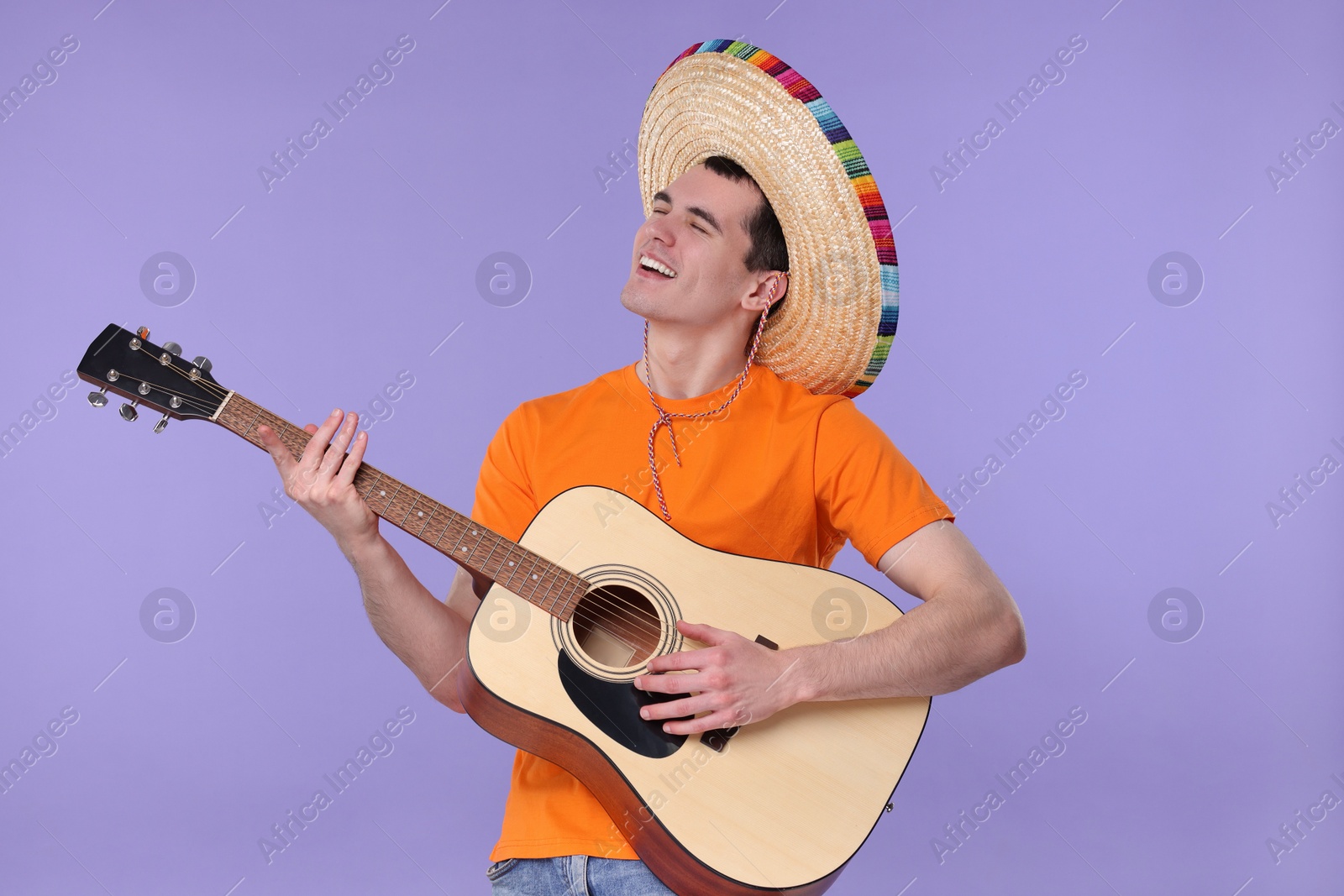 Photo of Young man in Mexican sombrero hat playing guitar on violet background