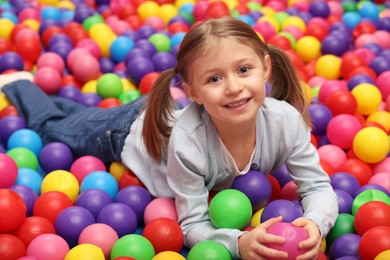 Photo of Happy little girl lying on many colorful balls in ball pit