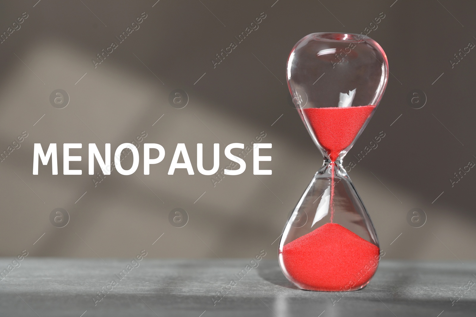 Image of Menopause word and hourglass on table against grey background