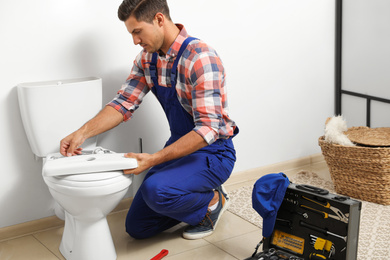 Photo of Professional plumber working with toilet bowl in bathroom