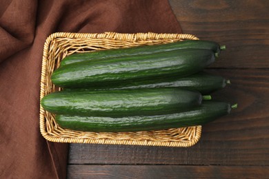 Photo of Fresh cucumbers in wicker basket on wooden table, top view