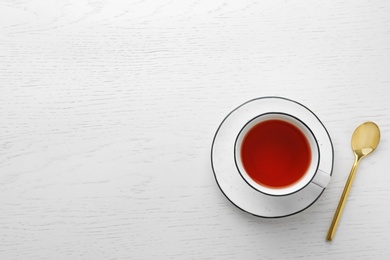 Cup of hibiscus tea with saucer and spoon on white wooden background, flat lay. Space for text