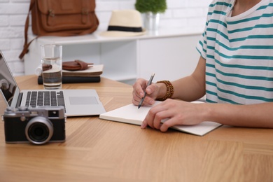 Photo of Woman with notebook planning trip at wooden table, closeup