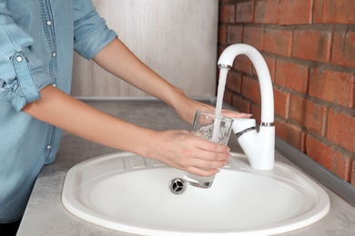 Woman filling glass with water from faucet in kitchen, closeup