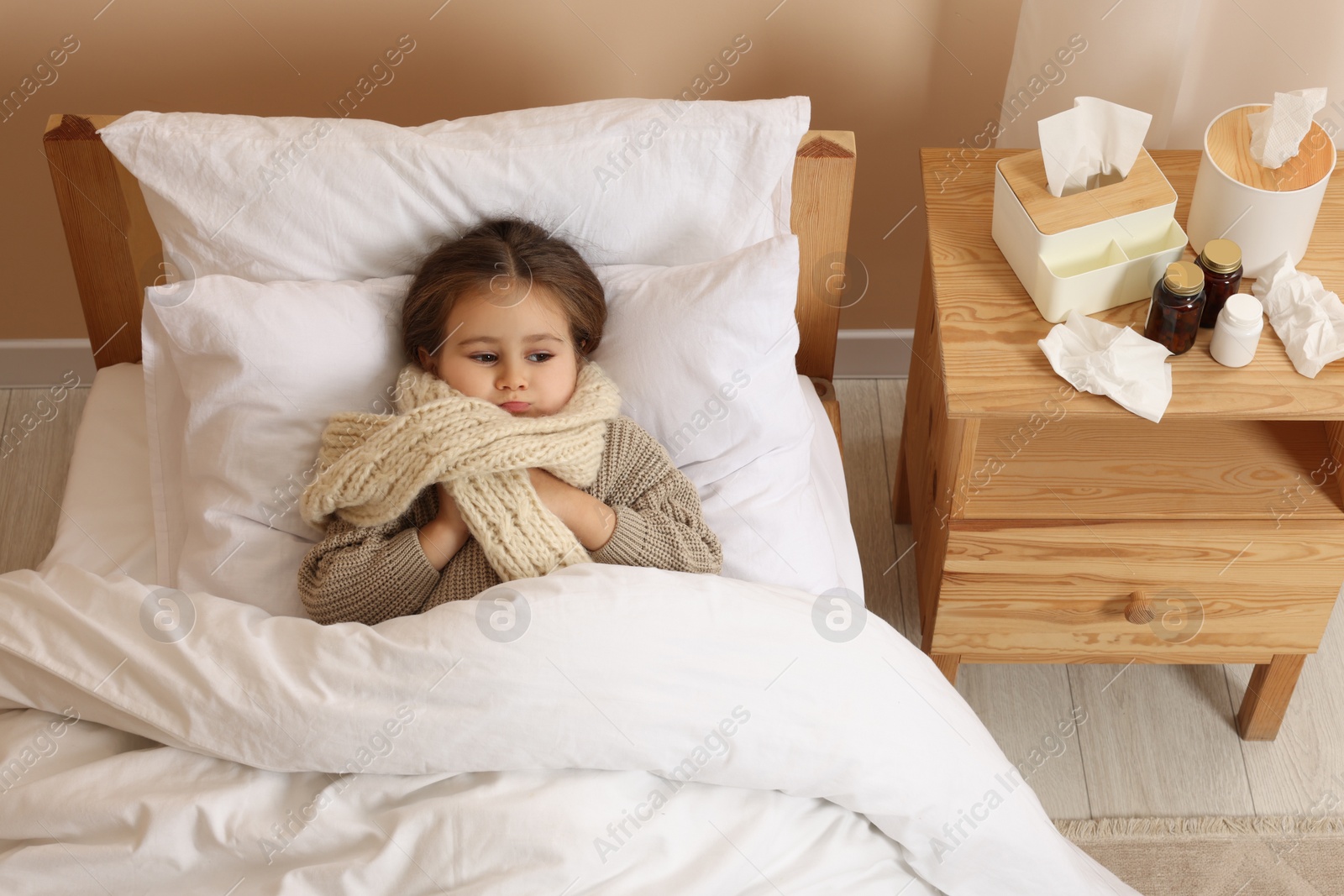 Photo of Sick girl with scarf around neck lying in bed at home, above view