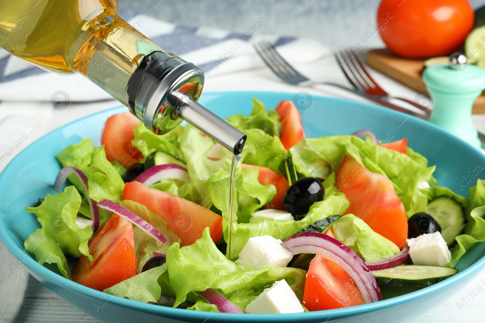 Photo of Adding cooking oil to delicious salad on table, closeup