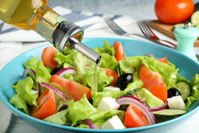 Photo of Adding cooking oil to delicious salad on table, closeup