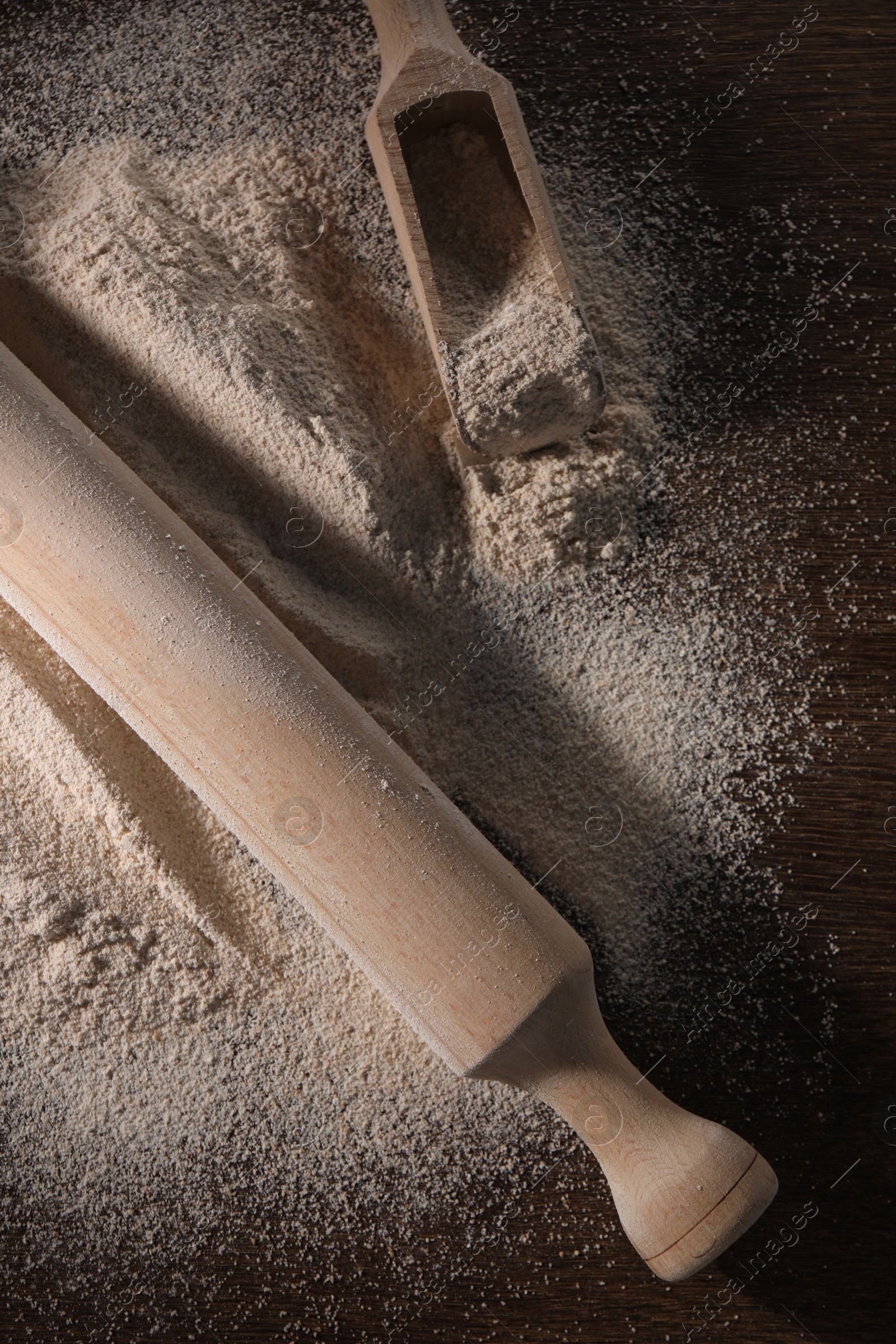 Photo of Pile of flour, rolling pin and scoop on wooden table, flat lay