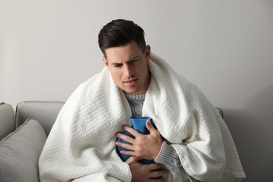 Photo of Ill man with hot water bottle suffering from cold at home